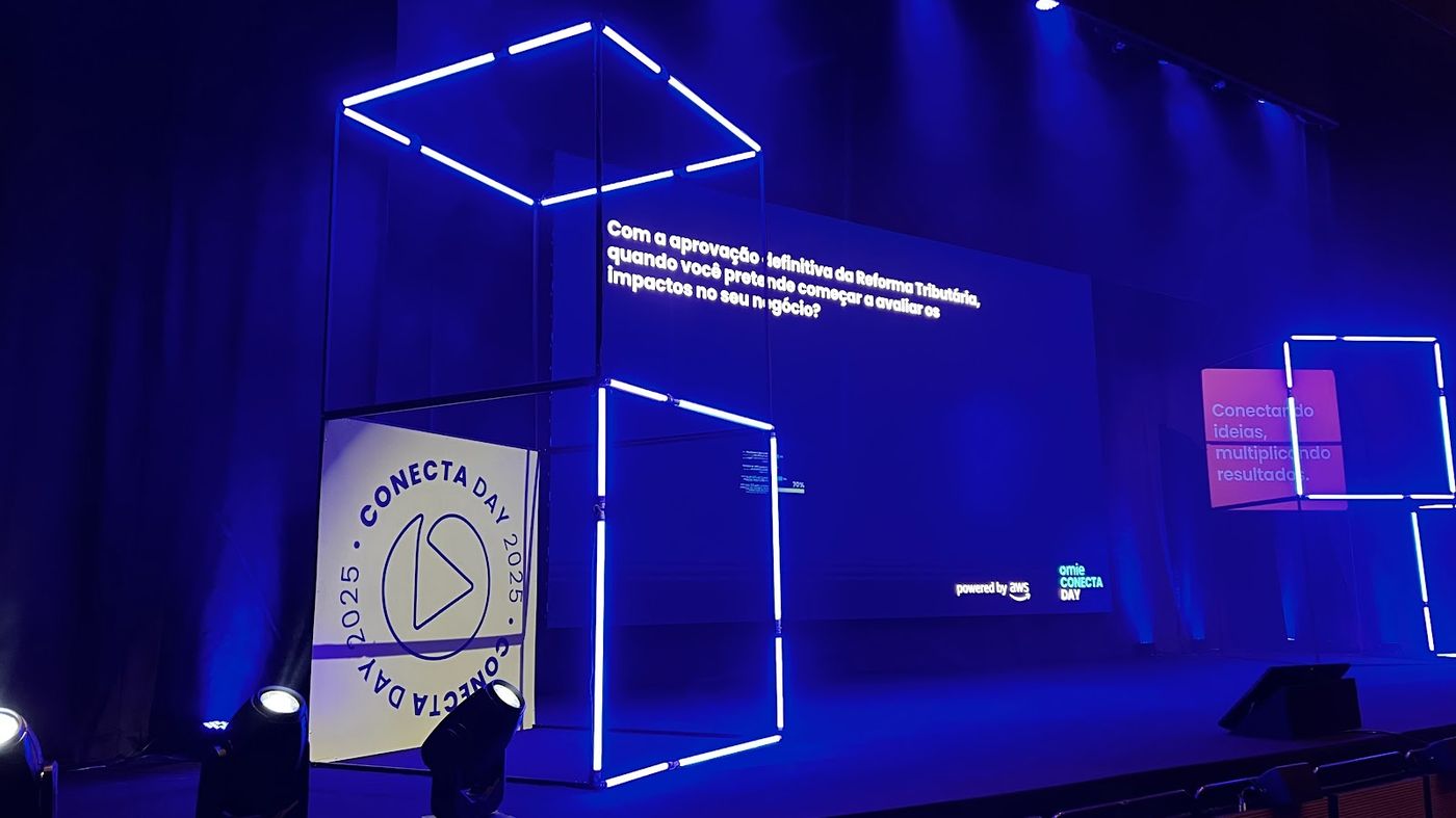 Cenografia de palco com cubo de neon, telão e iluminação azul em evento corporativo