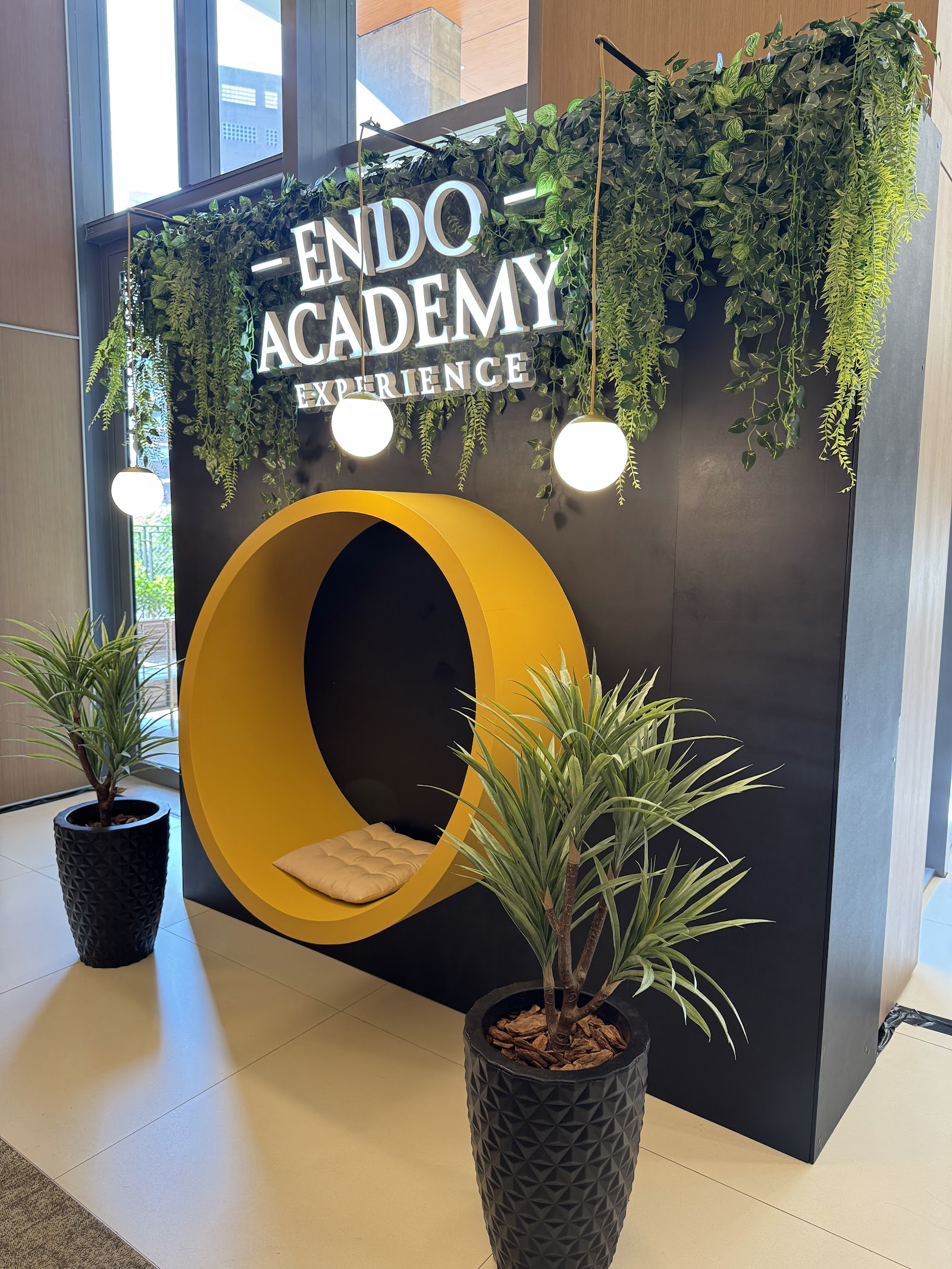 Cenário com assento circular, jardim suspenso e luminárias em evento acadêmico