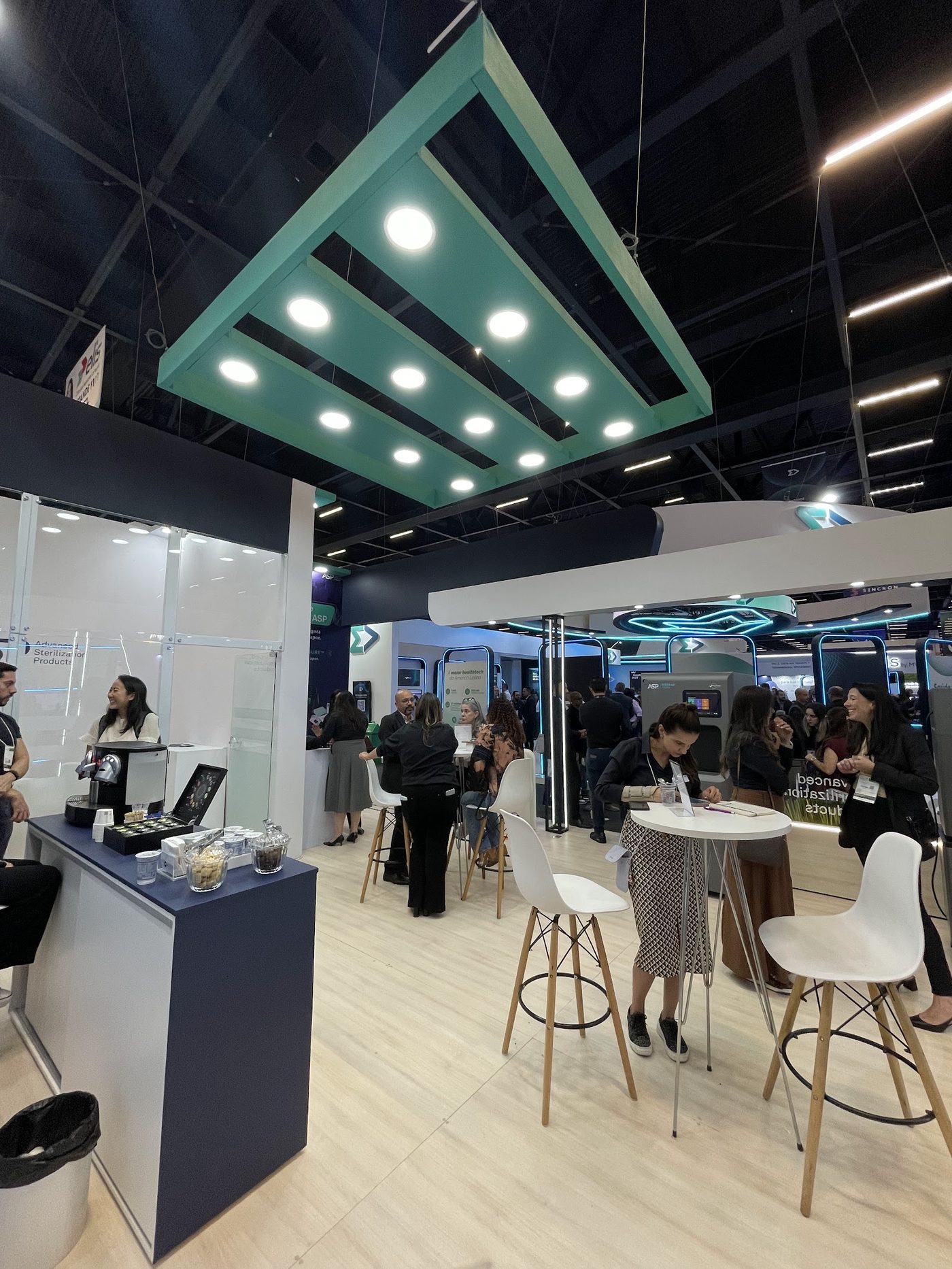 Stand com lounge, estrutura suspensa iluminada e mesas altas em pavilhão de feira