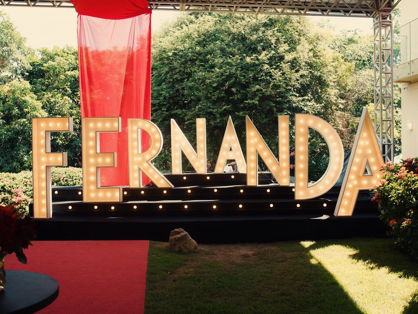 Letreiro luminoso com nome em jardim decorado para festa com tapete vermelho e estrutura treliçada