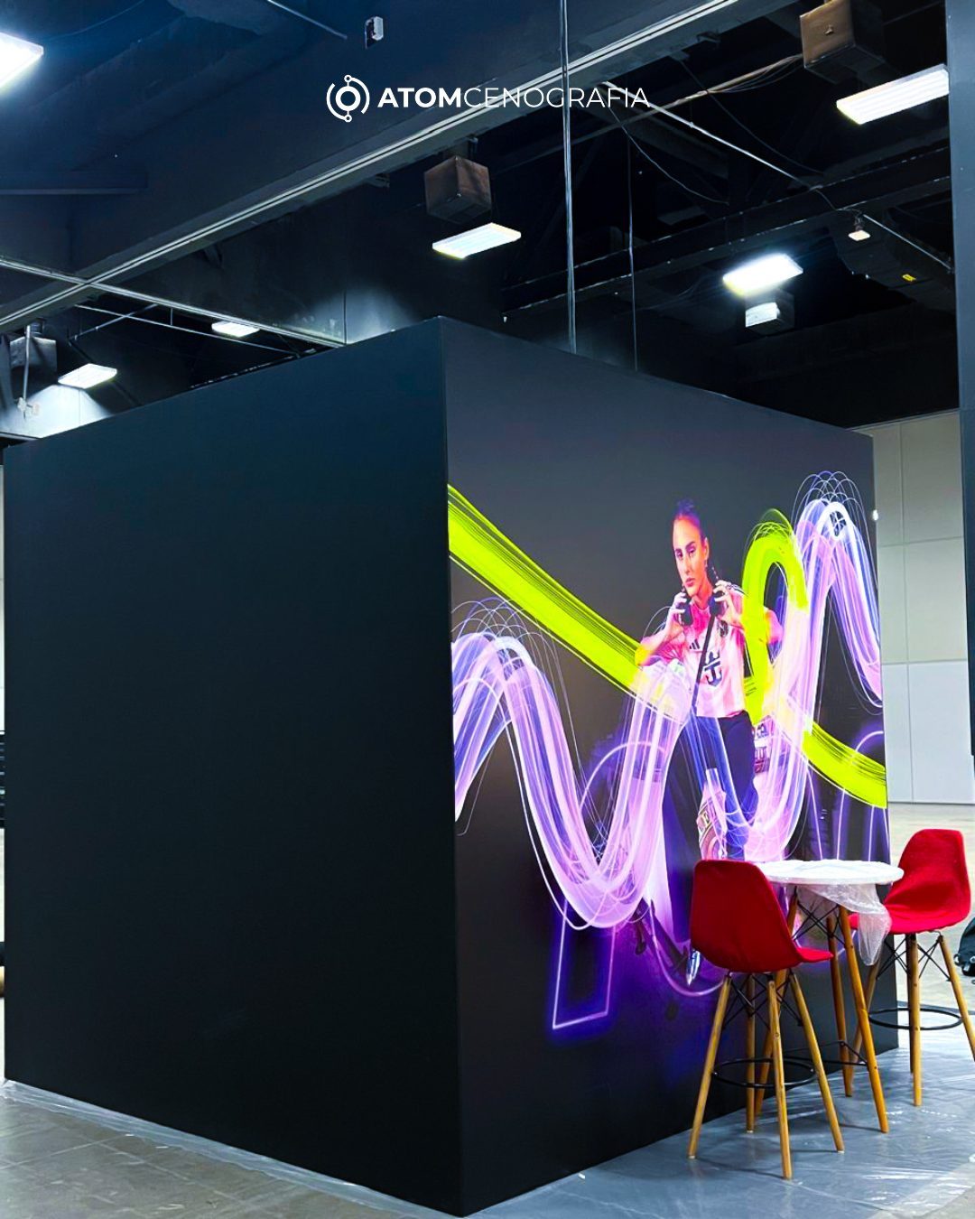 Estrutura cenográfica em cubo com arte neon e mesas vermelhas no stand Caixa Netshoes