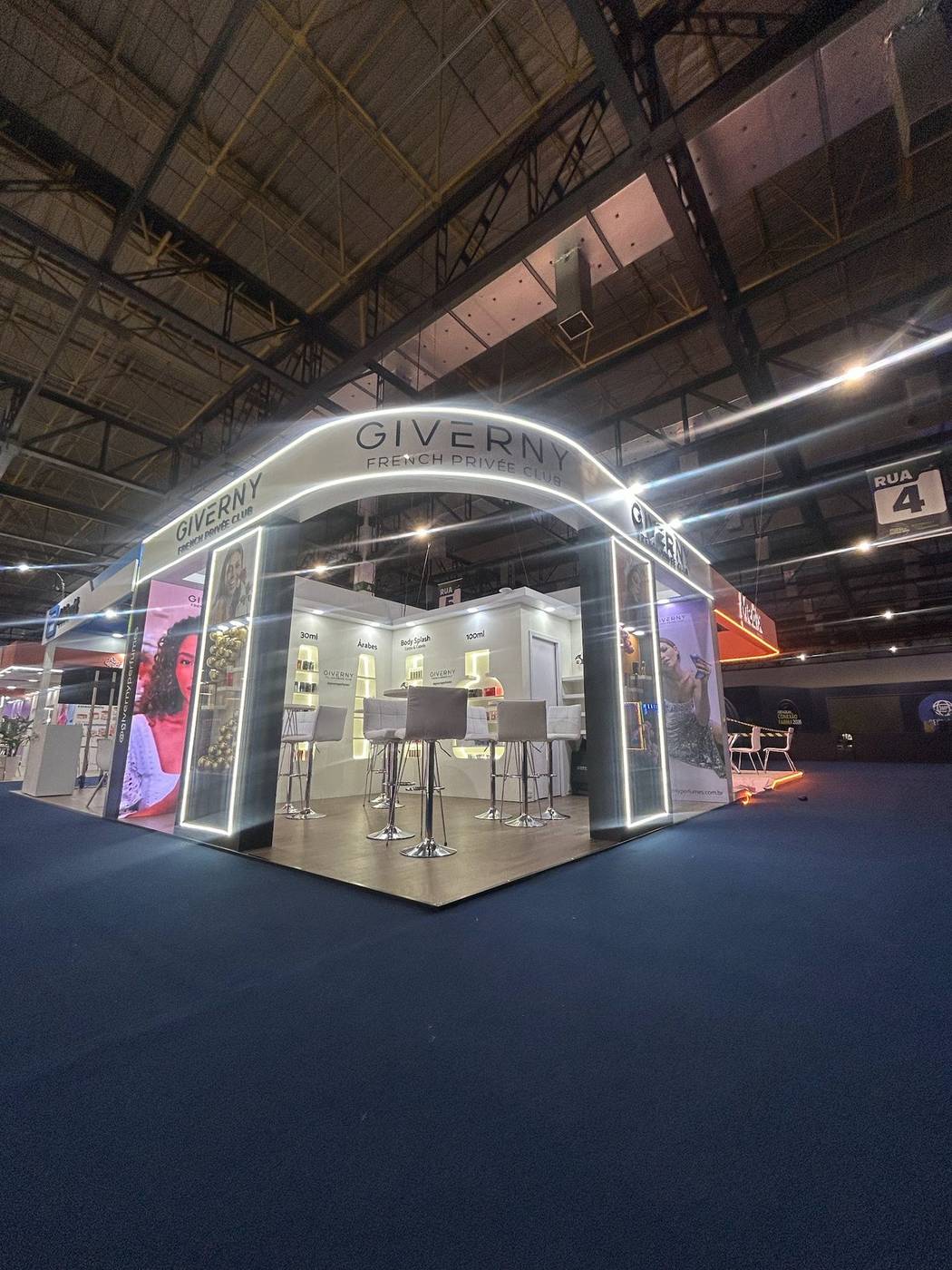 Stand de perfumaria em feira com pórtico arqueado, prateleiras e piso revestido