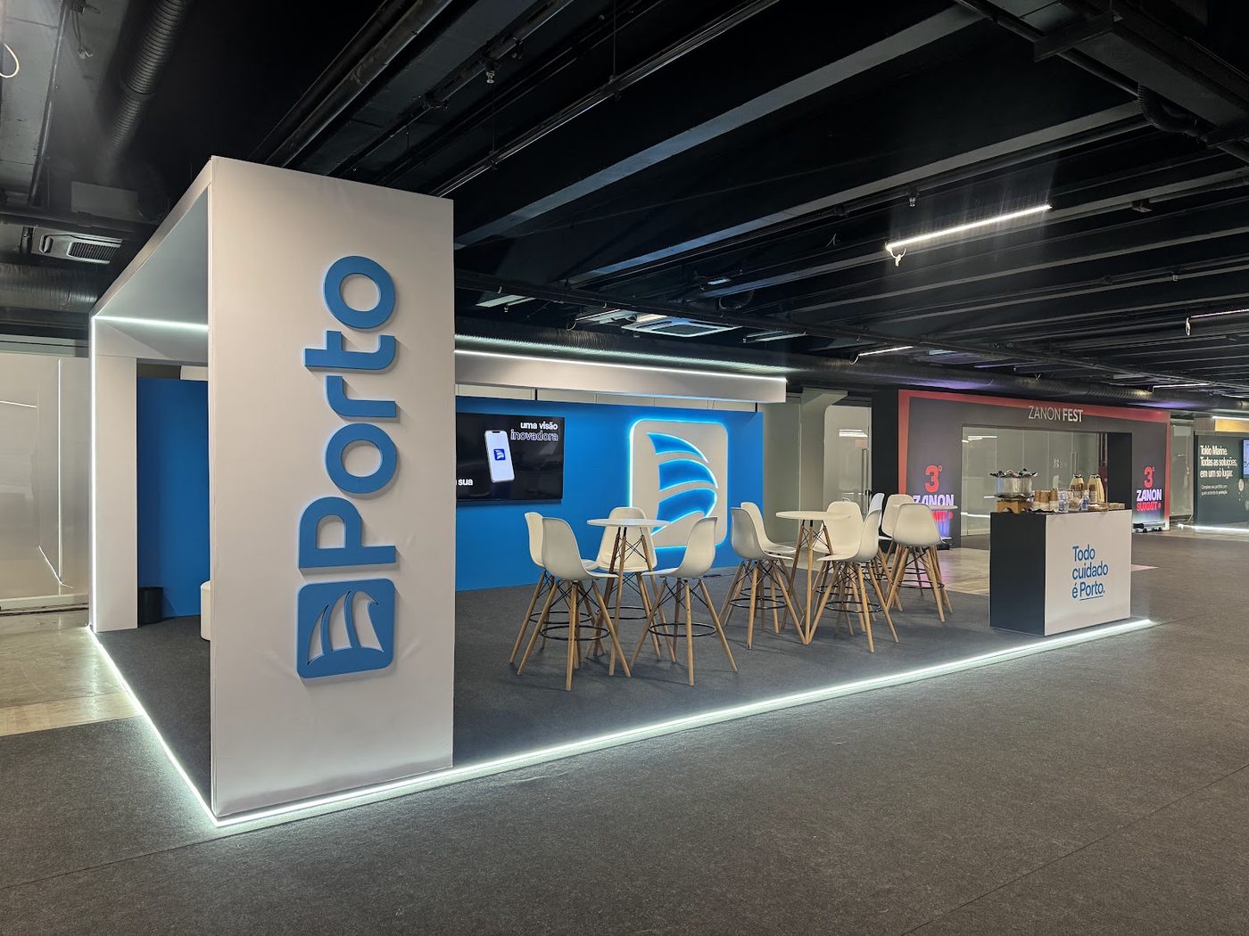 Stand de feira com painel azul iluminado e logotipo em relevo em ambiente corporativo