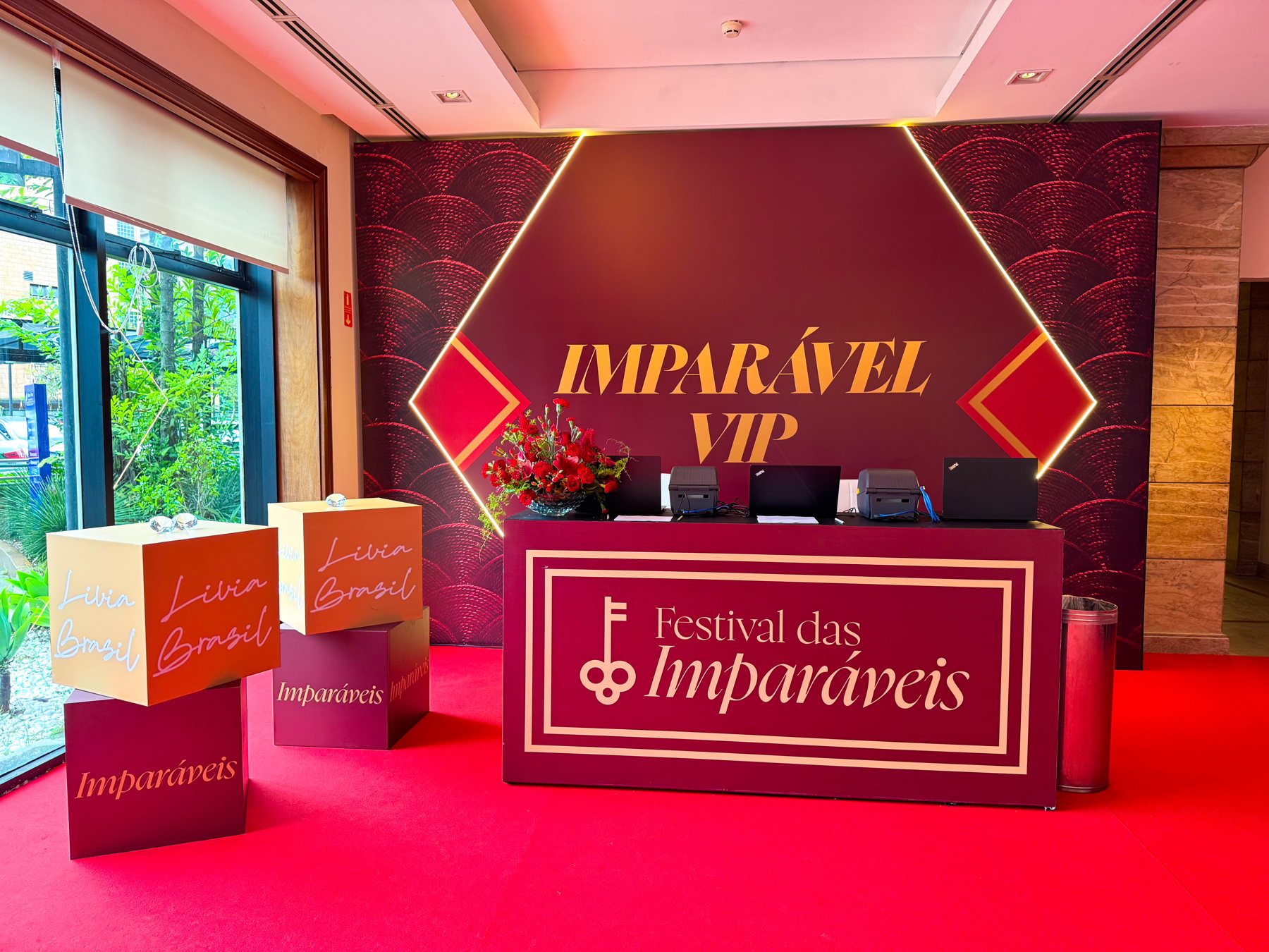 Backdrop com hexágono iluminado por perfil de LED e balcão com boiserie dourada e logo do Festival das Imparáveis